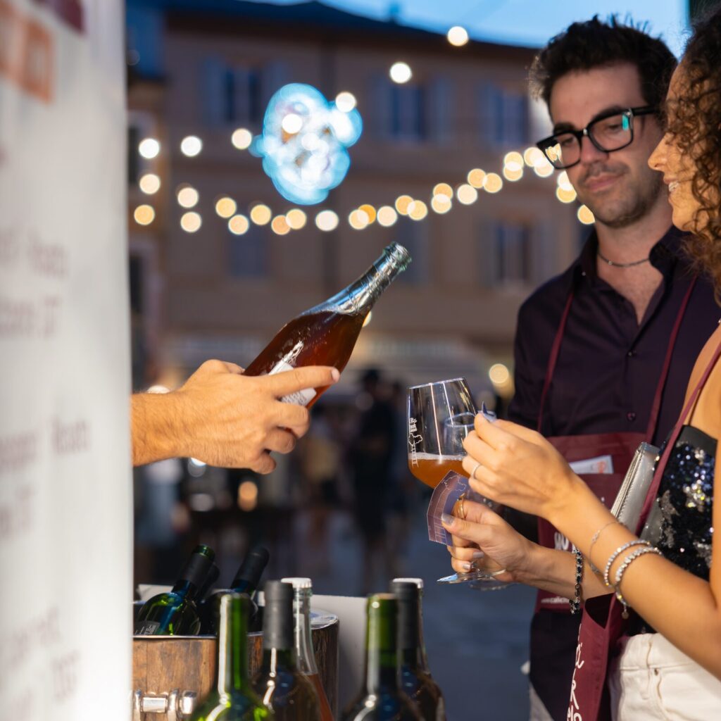 Un banco di degustazione con bottiglie e calici sotto le luci della piazza