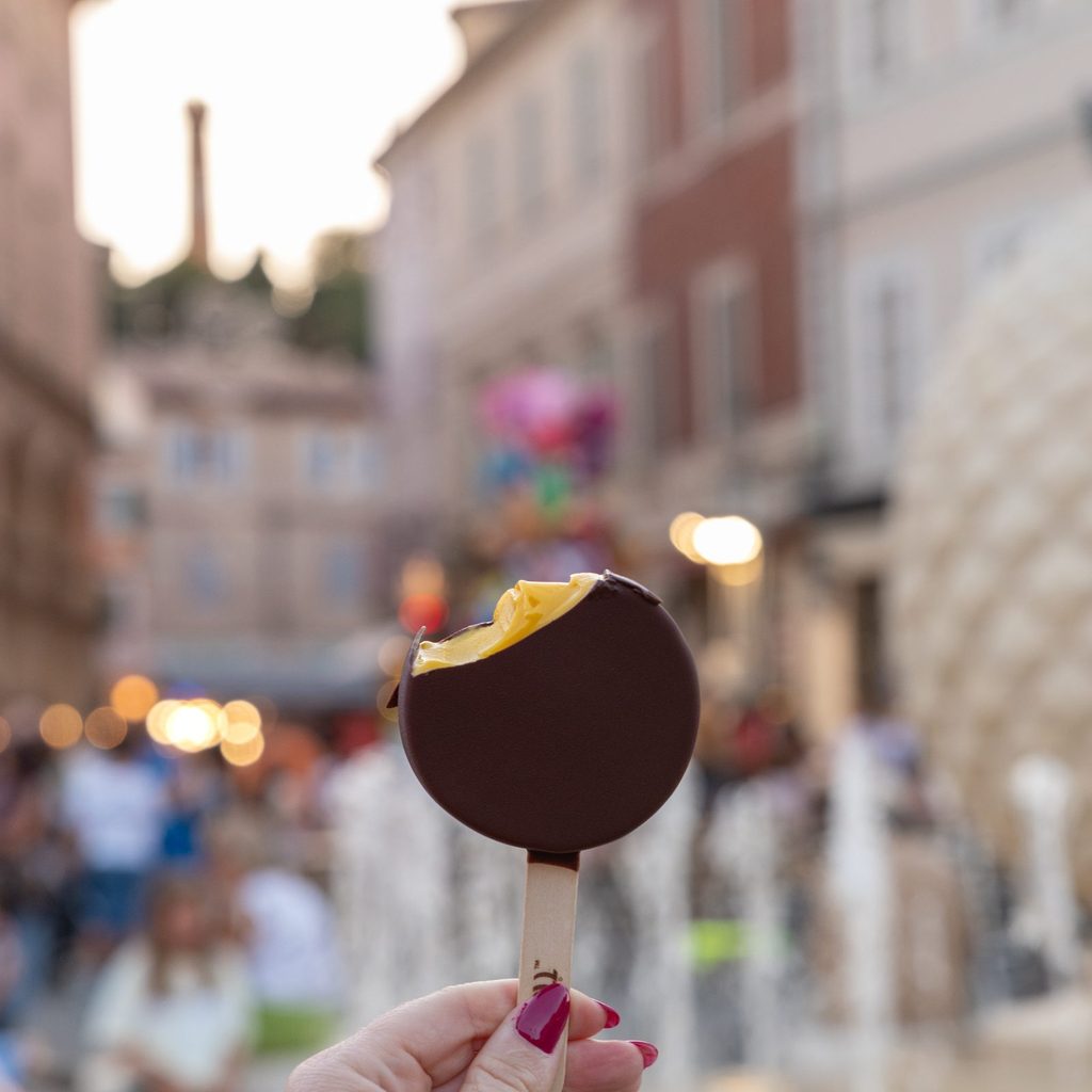 Gelato ricoperto di cioccolato con la piazza e la fontana sullo sfondo