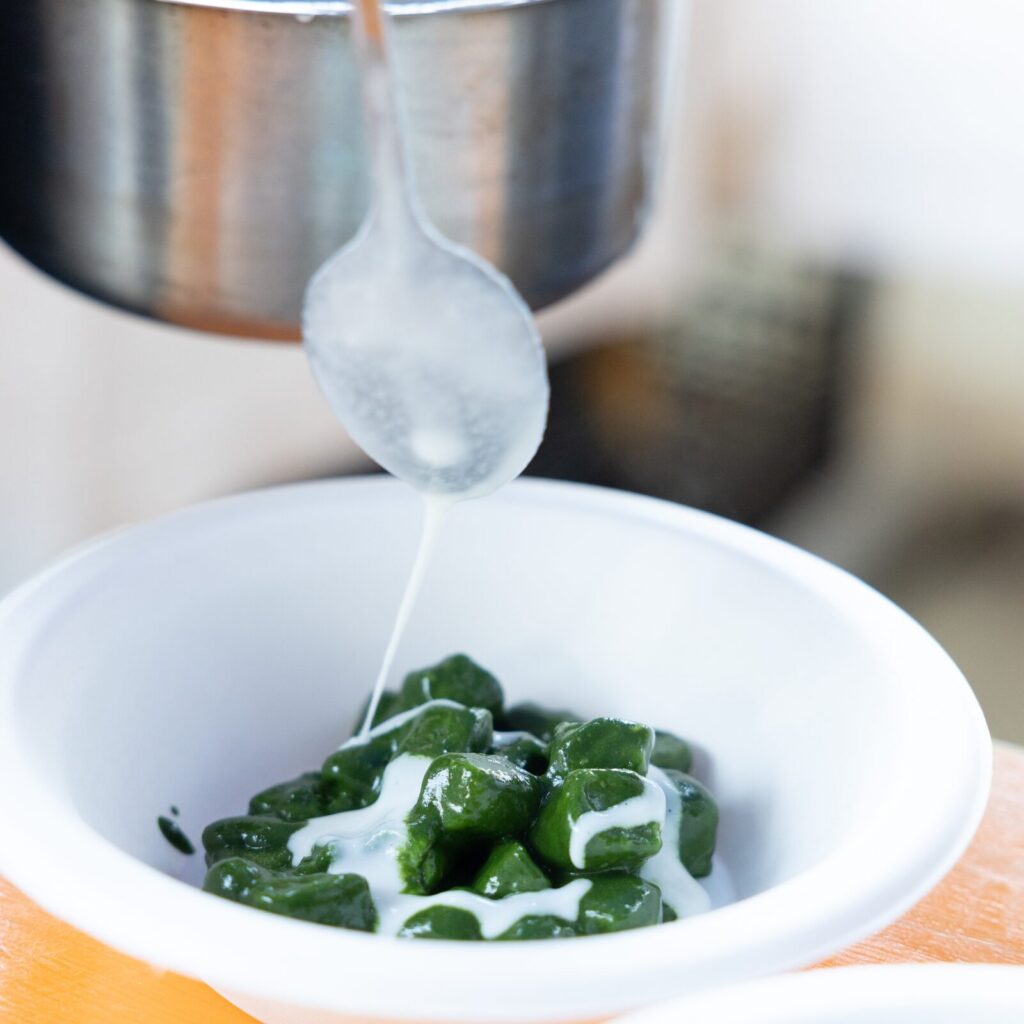 Gnocchi verdi in una ciotola con salsa versata al cucchiaio