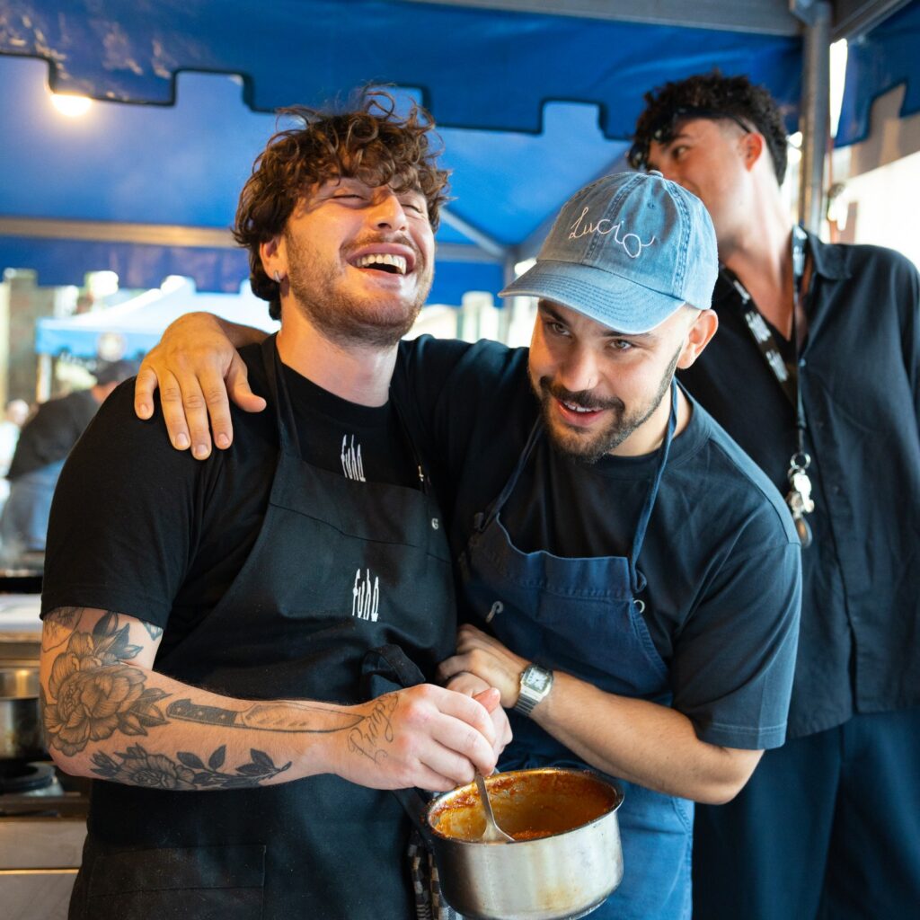 Due cuochi sorridenti a uno stand gastronomico mentre preparano un piatto