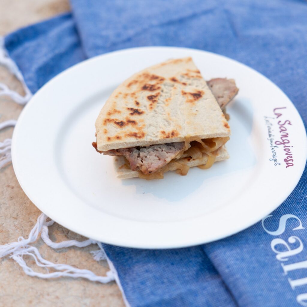 Piadina con salsiccia e cipolla servita in un piatto bianco su un tovagliolo blu