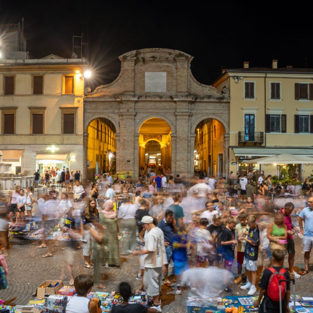 Mercatino serale in una piazza del centro storico di Rimini con gli archi storici illuminati