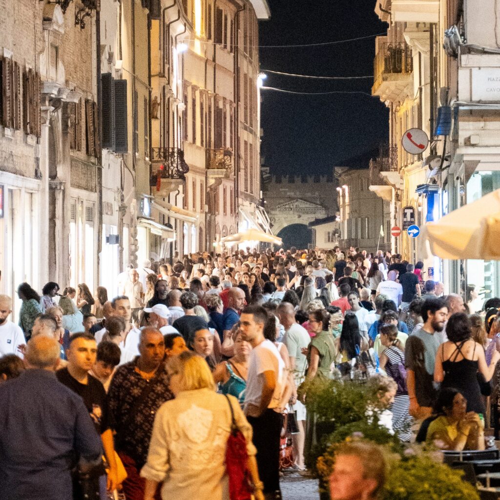 Il corso di Rimini affollato di sera durante la Shopping Night con l'arco monumentale sullo sfondo